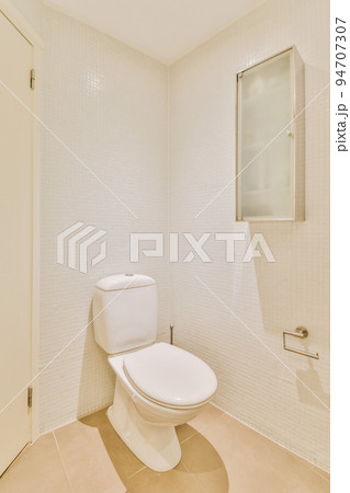 Interior of narrow restroom with sink and wall hung toilet with white walls and checkered floor 94707307