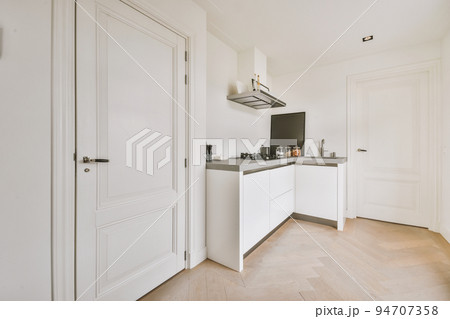 Fragment of interior of light narrow home kitchen with minimalist style white furniture with sink and stove Fragment of interior of light narrow home kitchen with minimalist style white furniture with sink and stove 94707358