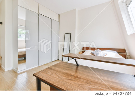 Home interior design of bedroom with bed and wooden wardrobe placed in corner near window in modern apartment 94707734