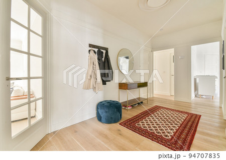 Narrow corridor with white walls and doors leading to spacious room with windows and parquet floor in modern apartment 94707835