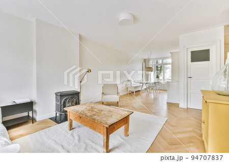 Shabby wooden table with chairs and vase located near comfortable couch against light walls with decorations in modern apartment 94707837
