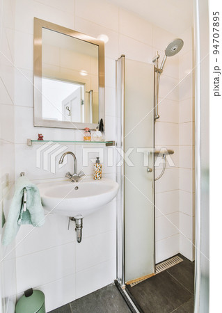 Sinks with mirrors and shower box with glass door in modern bathroom with white tiled walls Sinks with mirrors and shower box with glass door in modern bathroom with white tiled walls 94707895