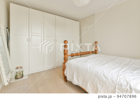 Home interior design of bedroom with bed and wooden wardrobe placed in corner near window in modern apartment Home interior design of bedroom with bed and wooden wardrobe placed in corner near window in modern apartment 94707896