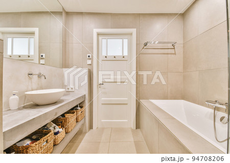 Sinks with mirrors and clean bathtub located near shower box with glass door in modern bathroom with white tiled walls Sinks with mirrors and clean bathtub located near shower box with glass door in modern bathroom with white tiled walls 94708206