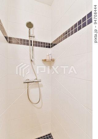Shower faucets attached to tiled wall near glass partition and ornamental curtail in washroom at home Shower faucets attached to tiled wall near glass partition and ornamental curtail in washroom at home 94708444