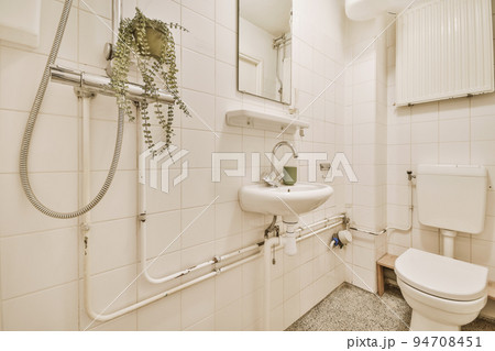 Interior of narrow restroom with sink and wall hung toilet with white walls and checkered floor 94708451