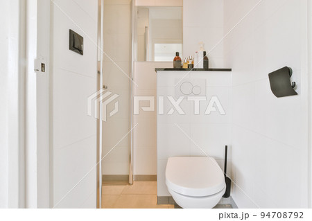 Interior of narrow restroom with sink and wall hung toilet with white walls and checkered floor Interior of narrow restroom with sink and wall hung toilet with white walls and checkered floor 94708792