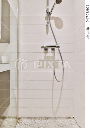 Shower faucets attached to tiled wall near glass partition and ornamental curtail in washroom at home 94708901