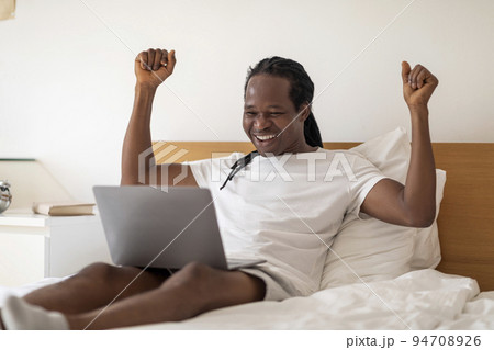 Great News. Joyful African American Man Celebrating Success With Laptop In Bed Great News. Joyful African American Man Celebrating Success With Laptop In Bed 94708926