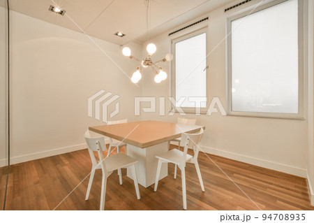 Table with chairs and flowers located near lounge area and kitchen in spacious room of contemporary apartment 94708935