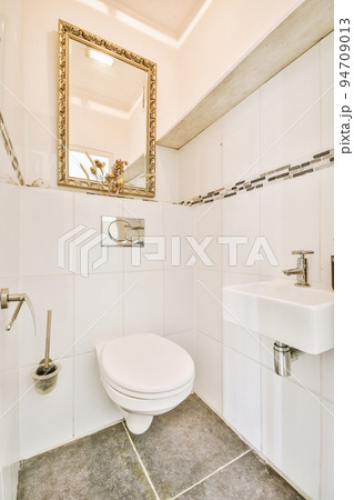 Interior of narrow restroom with sink and wall hung toilet with white walls and checkered floor Interior of narrow restroom with sink and wall hung toilet with white walls and checkered floor 94709013