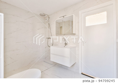 Modern flush toilet,shower box and ceramic sink installed on white tiled walls near mirror and towel in small restroom at home Modern flush toilet,shower box and ceramic sink installed on white tiled walls near mirror and towel in small restroom at home 94709245