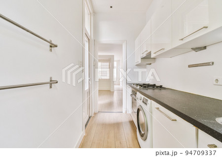 Well organized small home kitchen interior with sink under window and light furniture with stove and fridge in urban apartment 94709337