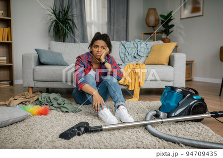 Unhappy tired young african american female sit on floor with vacuum cleaner, have problems with hygiene 94709435