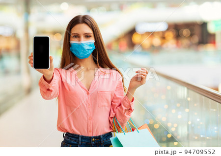 Lady Showing Cellphone Screen Shopping Wearing Face Mask In Hypermarket Lady Showing Cellphone Screen Shopping Wearing Face Mask In Hypermarket 94709552
