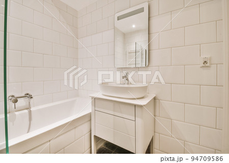 Sinks with mirrors and clean bathtub located near shower box with glass door in modern bathroom with white tiled walls Sinks with mirrors and clean bathtub located near shower box with glass door in modern bathroom with white tiled walls 94709586