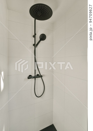 Shower faucets attached to tiled wall near glass partition and ornamental curtail in washroom at home 94709627