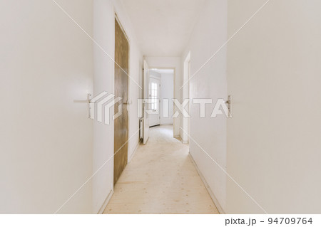 Light narrow hallway with many doors in white walls and glowing lamp over lumber floor 94709764