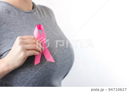 Woman in gray t-shirt attaches pink ribbon to her chest. Breast Cancer Awareness Month. Promoting campaign against cancer. Woman in gray t-shirt attaches pink ribbon to her chest. Breast Cancer Awareness Month. Promoting campaign against cancer. 94710627