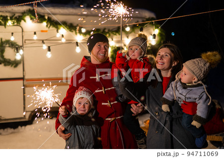 Happy family celebrates christmas in nature and holds sparklers. Parents with three sons travels in a van. 94711069
