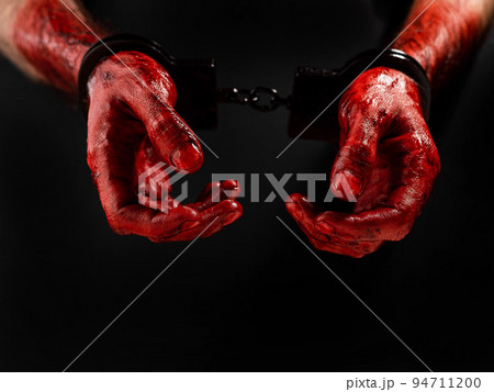 Close-up of male bloody handcuffed hands on a black background. 94711200