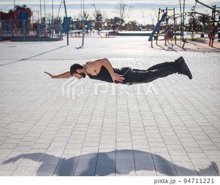 A man in black sportswear jumps doing push-ups in the park. 94711221