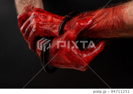 Close-up of male bloody handcuffed hands on a black background. Close-up of male bloody handcuffed hands on a black background. 94711251