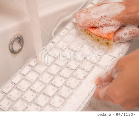 Woman washing white computer keyboard with a sponge with foam. 94711507