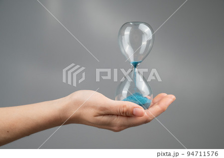 Woman holding an hourglass on a gray background. Close-up. 94711576