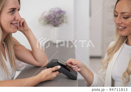 A young woman pays in a beauty salon with a credit card using NFC contactless payment. A young woman pays in a beauty salon with a credit card using NFC contactless payment. 94711813