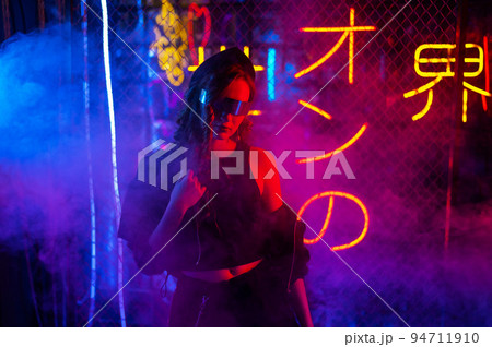Caucasian woman in sunglasses posing in fog in neon studio. 94711910
