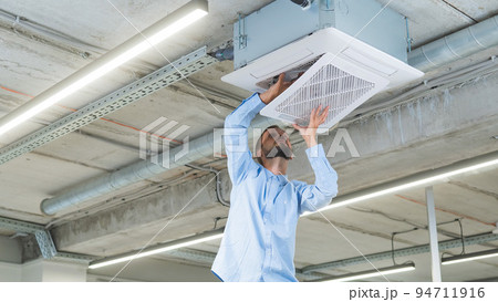 Caucasian bearded man repairing the air conditioner in the office. Caucasian bearded man repairing the air conditioner in the office. 94711916