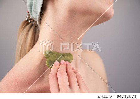 Close-up portrait of a young woman massaging her neck with a gouache scraper. Close-up portrait of a young woman massaging her neck with a gouache scraper. 94711971