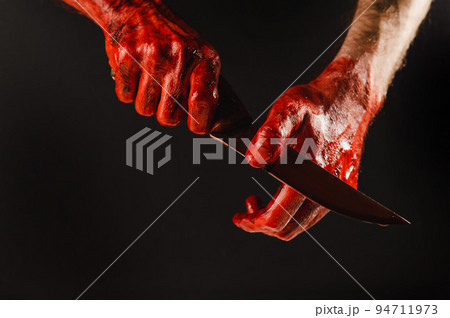 A man wipes a bloody knife with his hand on a black background. A man wipes a bloody knife with his hand on a black background. 94711973