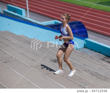 Young caucasian woman running on stadium stairs outdoors. Young caucasian woman running on stadium stairs outdoors. 94712036