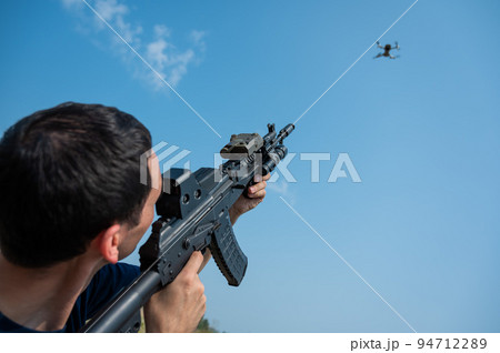 Caucasian man shoots a flying drone with a rifle. Caucasian man shoots a flying drone with a rifle. 94712289