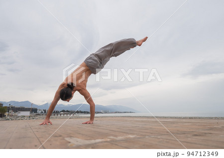 Shirtless caucasian man doing backflip on pebble beach.  94712349