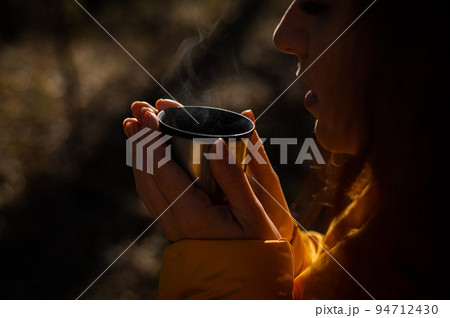 A woman holds a thermos of hot tea in her hands on a cold autumn day. 94712430