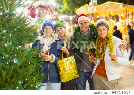 Portrait of man and woman and their happy teenagers posing with paper bags near counters at Christmas fair Portrait of man and woman and their happy teenagers posing with paper bags near counters at Christmas fair 94713914