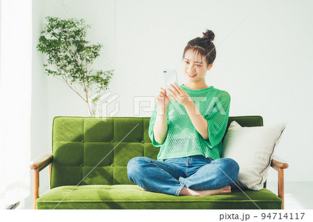 ソファに座ってスマホを見る女性 94714117