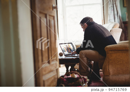 Senior man sitting on sofa using laptop having video call Senior man sitting on sofa using laptop having video call 94715769