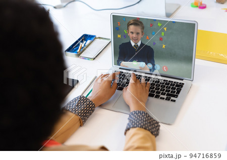 Mixed race female teacher using laptop on video call with schoolboy learning from home 94716859