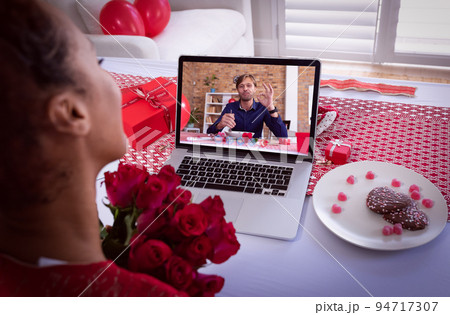 Diverse couple making valentines date video call the man on laptop screen eating and woman holding f Diverse couple making valentines date video call the man on laptop screen eating and woman holding f 94717307