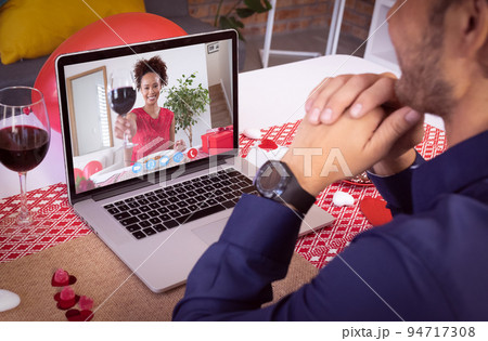 Diverse couple making valentine's date video call the woman on laptop screen raising glass of wine Diverse couple making valentine's date video call the woman on laptop screen raising glass of wine 94717308
