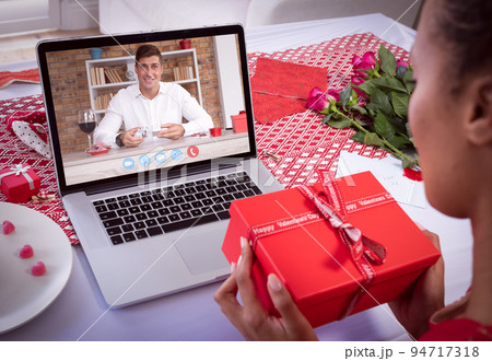 Diverse couple making valentine's date video call using laptop both holding gifts Diverse couple making valentine's date video call using laptop both holding gifts 94717318