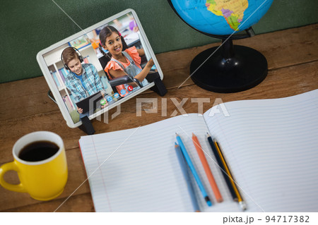 School children learning displayed on tablet screen placed on desk with notebook during video call School children learning displayed on tablet screen placed on desk with notebook during video call 94717382