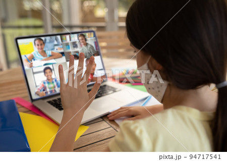 Caucasian schoolgirl wearing face mask, using laptop and waving on video call with school friends Caucasian schoolgirl wearing face mask, using laptop and waving on video call with school friends 94717541