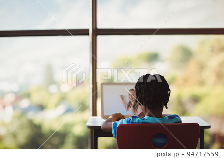 Rear view of male student having a video call with female teacher on laptop at school Rear view of male student having a video call with female teacher on laptop at school 94717559
