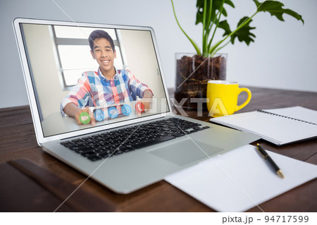 Mixed race schoolboy learning displayed on laptop screen placed on desk during video call 94717599
