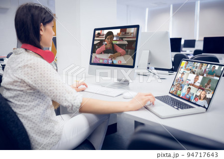 Caucasian female teacher using computer and laptop on video call with school children 94717643